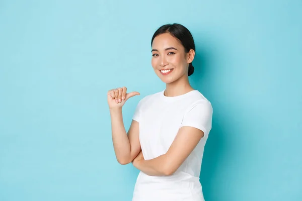 Confiada sonriente chica asiática en camiseta blanca apuntándose a sí misma con expresión orgullosa y asertiva, presumiendo, promoviendo sus propias habilidades, siendo profesional, buscando trabajo, de pie fondo azul —  Fotos de Stock