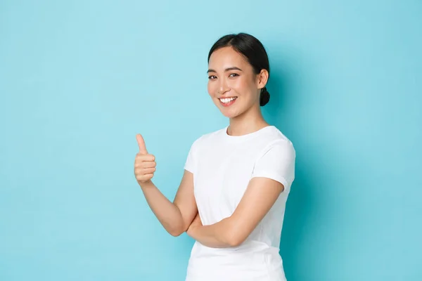 Πορτρέτο της αυτοπεποίθηση χαρούμενος χαμογελαστός, όμορφο κορίτσι της Ασίας σε λευκό t-shirt δείχνει τον αντίχειρα-up στην έγκριση, ενθαρρύνει να κάνουμε κάτι, να δώσει την άδεια, αναζητούν ευχαριστημένοι πάνω από το μπλε φόντο — Φωτογραφία Αρχείου