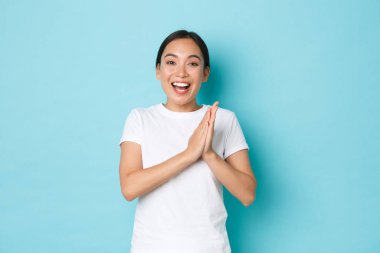 Gülümseyen, mutlu ve mutlu Asyalı kız, biri için seviniyor. Ellerinizi çırpın ve kazanarak ya da zaferle kişiyi tebrik edin. Mavi arka plandan memnun görünüyor.