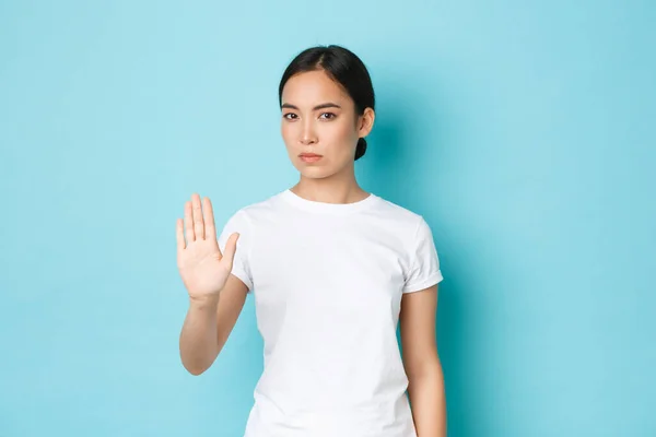 Wanita asia yang percaya diri serius menghentikan sesuatu yang buruk, mengangkat tangan dalam larangan, tidak setuju atau melarang isyarat, berdiri latar belakang biru dan menolak tawaran yang buruk, menolak — Stok Foto