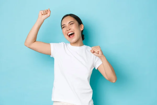 Regocijándose mujer asiática feliz celebrando la victoria. Chica eufórica triunfando sobre el logro, bomba de puño y gritando sí encantado, de pie animado y confiado, fondo azul — Foto de Stock