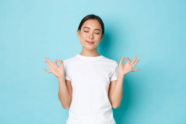 Porträtt av glad lugn och tålmodig asiatisk kvinna med slutna ögon, leende nöjd, hålla händerna i sidled i Lotus pose, nå nirvana, lugna ner under meditation, blå bakgrund — Stockfoto