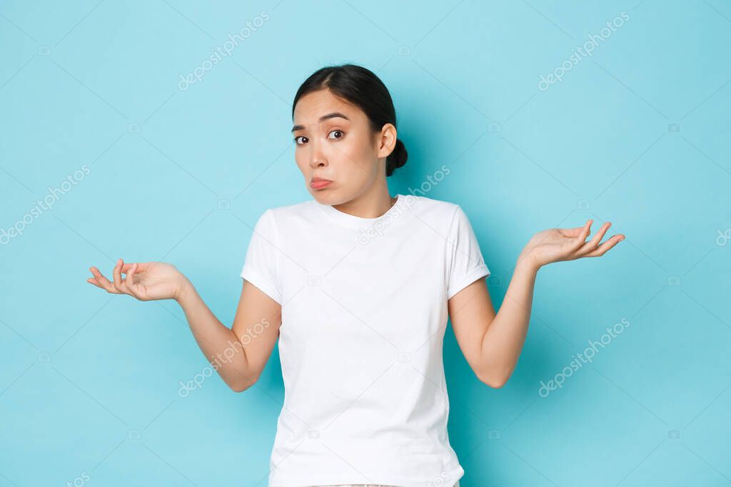 Confused and indecisive cute asian girl grimacing while cant figure out something, raising hands clueless and shrugging puzzled, dont know anything, standing blue background