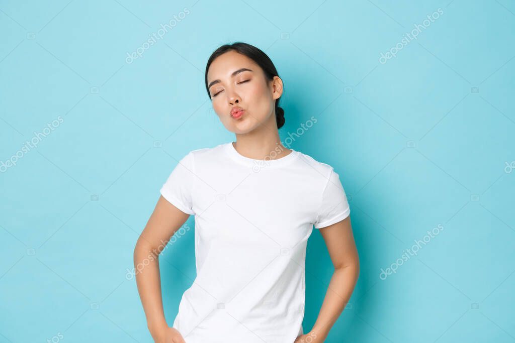 Silly and cute asian girl close eyes and dreamy pouting, waiting or imaging romantic kiss, looking lovely over blue background in casual white t-shirt, lifestyle and people concept