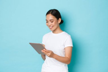 Gülümseyen güzel Asyalı kız, üç boyutlu kadın sanatçı veya serbest çalışan dijital tablet kullanan ve cihaz ekranına, online alışverişe ya da açık mavi arka planda gezinmeye bakan kişinin portresi
