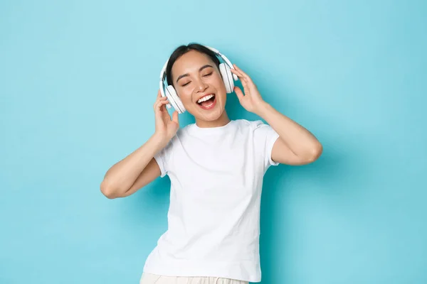 Concepto de compras, dinero y finanzas. Upbeat chica asiática en blanco casual camiseta, cantando karaoke, reproducción de música aplicación, escuchar música en auriculares inalámbricos y disfrutar de un sonido perfecto — Foto de Stock