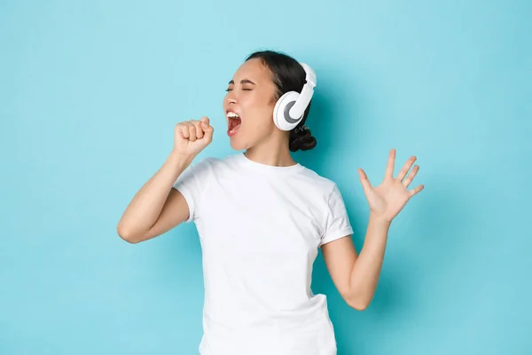 Conceito de compras, dinheiro e finanças. Upbeat menina asiática em branco casual t-shirt, karaoke cantando, tocando aplicativo de música, ouvir música em fones de ouvido sem fio e desfrutar de som perfeito — Fotografia de Stock