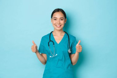 Covid-19, sosyal uzaklık ve koronavirüs salgını konsepti. İyimser ve destekleyici Asyalı kadın doktor, hemşire her şeyi teşvik et tamam mı? Onaylanmış ve gülümseyen, önlük giymiş.