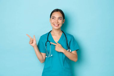 Covid-19, sosyal uzaklık ve koronavirüs salgını konsepti. Neşeli gülümseyen Asyalı kadın hemşire, önlüklü doktor sol üst köşeyi işaret ediyor ve klinik reklamına bakıyor.