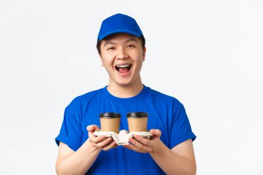 Çevrimiçi siparişler, paket servis ve çalışanlar konsepti. Neşeli gülümseyen Asyalı erkek kuryenin yakın çekimi, teslimatçı müşteriye kahve götürmekten mutlu, beyaz arka planda duran