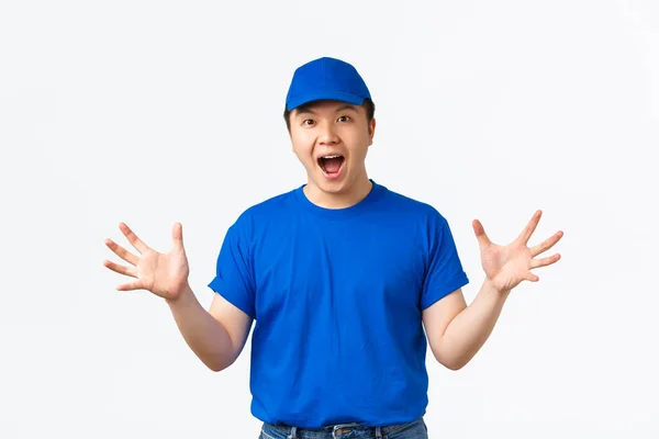 Portrait of excited and euphoric asian delivery man in blue uniform react to wonderful news, shaking hands happy and thrilled, telling big announcement, rejoicing over white background — Stock Photo, Image