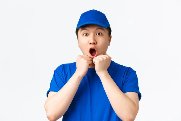 Online shopping, fast shipping, employees and home delivery concept. Excited and speechless, emotive asian male courier in blue uniform, reacting to awesome news, gasping amazed, white background — Stock Photo, Image