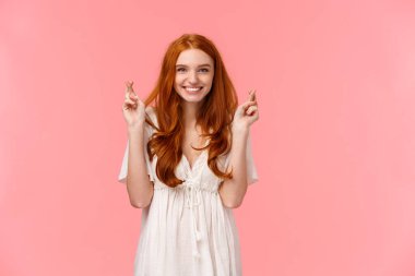 Kendine güvenen, iyimser ve umut dolu beyaz elbiseli, umut dolu kızıl saçlı kadın, şans dileyin ve gülümseyin, dilek tutun, beklenen rüyayı gerçekleştirin, pembe arka planda durun.