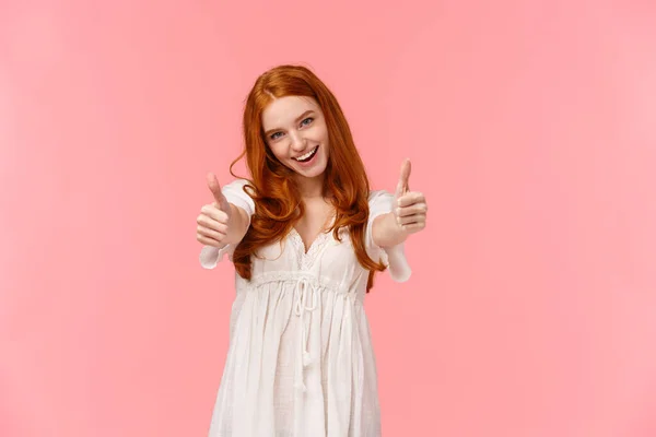 Támogatom a döntésed. Karizmatikus izgatott, boldog vörös hajú nő fehér ruhában, mutatja hüvelykujját-up, hogy felvidítsa, egyetért vagy kifejezni elégedettségét hűvös termék, mosoly jóváhagyása, rózsaszín háttér — Stock Fotó