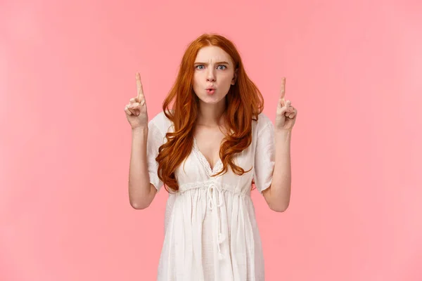 What the hell is that. Mad and displeased, intense redhead girlfriend asking for explanation as seeing outrageous situation, pointing fingers up, frowning angry, standing pink background — 스톡 사진