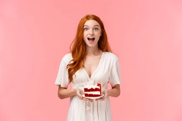Surprised and amused charismatic redhead girl gossiping during party, holding plate with cake and open mouth fascinated as talking on birthday event, standing pink background
