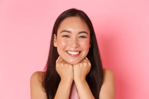 Beauté, mode et style de vie concept. Gros plan de magnifique fille asiatique heureuse, à la recherche rêveuse et ravie, la tête penchée sur les mains et souriant insouciant avec des dents blanches, debout fond rose — Photo