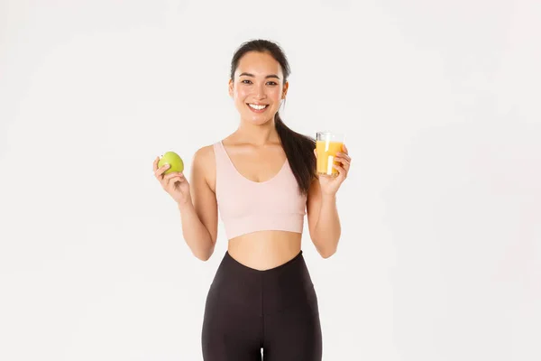 Esporte, bem-estar e conceito de estilo de vida ativo. Retrato de saudável e se encaixa bem-parecido asiático esportista segurando suco de laranja e maçã, café da manhã antes do treino, fundo branco — Fotografia de Stock