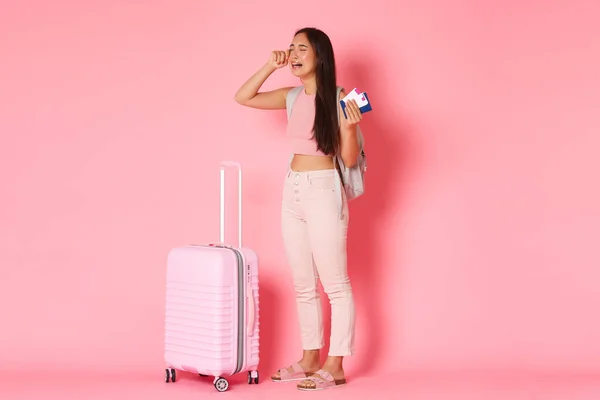 Reisen, Urlaub und Urlaubskonzept. Ganztägig weinende, traurige und verzweifelte asiatische Touristinnen, fühlen sich deprimiert über den verpassten Flug, wischen sich Tränen ab, stehen neben dem Koffer vor rosa Hintergrund — Stockfoto