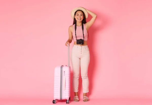 Tourismus, Sommerurlaub, Urlaub im Ausland. Volle Länge attraktive asiatische Mädchen erkunden neue Länder, trägt Sommerkleidung, steht mit Koffer und Kamera, rosa Hintergrund — Stockfoto