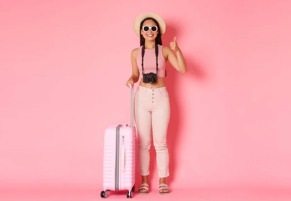 Tourismus, Sommerurlaub, Urlaub im Ausland. Volle Länge der schönen entspannten asiatischen Mädchen Touristin, Reisende in Sonnenbrille und Sommerkleidung zeigen Daumen nach oben, wie Hotel, rosa Hintergrund — Stockfoto