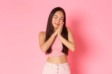 Yaşam tarzı, güzellik ve kadın konsepti. Mutlu ve mutlu, uykulu Asyalı bir kızın portresi güzel bir şeyin hayalini kuruyor. Avuç içlerine uzanmış, gözleri kapalı, pembe arka planda uyuyor.