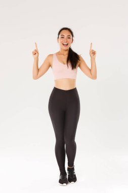 Spor, spor salonu ve sağlıklı vücut konsepti. Neşeli, gülümseyen Asyalı fitness kızı, spor giyimli bayan sporcu reklamı gösteren, parmaklarını havaya kaldıran ve antrenman için davet eden,
