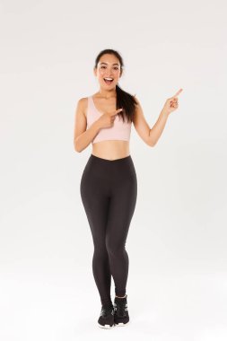 Tam boy arsız çekici bayan sporcu, spor giyimli Asyalı fitness kızı sağ üst köşeyi işaret ediyor, tanıtım yapıyor, egzersiz malzemeleri satışı, fitness eğitimi indirimi gösteriyor.