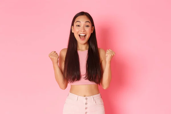 Lifestyle, beauty and women concept. Successful winning pretty asian girl reacting to exciting news, fist pump and screaming yes while triumphing, celebrate victory or achievement, pink background — Stock Photo, Image