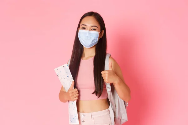 Safe tourism, travelling during coronavirus pandemic and preventing virus concept. Cheerful cute asian girl tourist encourage social distance while travel abroad, show thumbs-up and wear medical mask — Stock Photo, Image