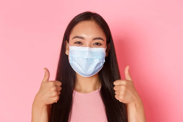 Safe tourism, travelling during coronavirus pandemic and preventing virus concept. Close-up of pleased, cheerful asian girl tourist in medical mask showing thumbs-up, like her vacation — Stock Photo, Image