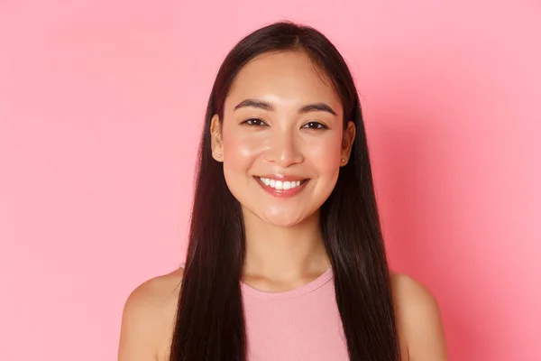 Conceito de beleza, moda e estilo de vida. Close-up de bela menina asiática feliz com sorriso branco perfeito, olhando otimista, de pé esperançoso e otimista sobre fundo rosa — Fotografia de Stock