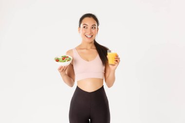 Spor, refah ve aktif yaşam tarzı konsepti. Gülümseyen fitness kızı, sol üst köşeye bakan Asyalı bayan sporcu mutlu, egzersiz yapmadan önce sağlıklı salata ve portakal suyu yiyor, diyetle kilo veriyor.