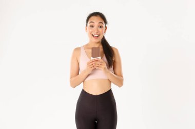 Spor, refah ve aktif yaşam tarzı konsepti. Mutlu gülümseyen Asyalı bayan sporcu çikolatalı proteini kötü tutuyor ve heyecanlı görünüyor, uzun süre egzersiz yapmak için sağlıklı tatlılar yiyor.