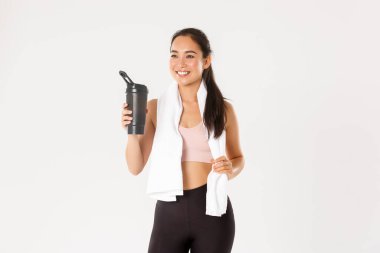 Spor, refah ve aktif yaşam tarzı konsepti. Tatmin olmuş gülümseme, sağlıklı ve ince Asya fitness koçu, kız iyi eğitimden, içme suyundan veya proteinden ve havluyu tutmaktan memnun.