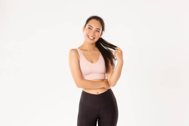 Spor, refah ve aktif yaşam tarzı konsepti. Spor kıyafetli güzel Asyalı kız, at kuyruğuyla oynuyor ve spor salonundan sonra kameraya mutlu görünüyor, beyaz arka planda duruyor.