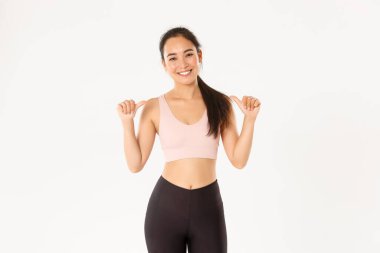 Spor, refah ve aktif yaşam tarzı konsepti. İnce ve güçlü gülümseyen, çekici Asyalı kadın fitness koçu, kişisel eğitmen ya da antrenör kendini gösteren spor salonu logonuz, beyaz arka plan.