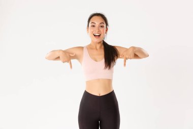 Spor, refah ve aktif yaşam tarzı konsepti. Gülümseyen enerjik Asyalı fitness kızı, etkinliğe davet edilen bayan sporcu, egzersiz vitesi reklamını gösteren, parmaklarını aşağıya gösteren, logo pankartın.