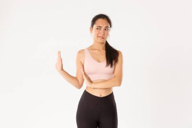 Spor, refah ve aktif yaşam tarzı konsepti. Tatminsiz ve eğlendirilmemiş Asyalı fitness kızı eliyle bloğu gösteriyor ve sola bakıyor, tiksinti duyuyor ve kötü bir şeyi reddediyor.