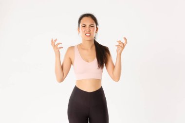 Spor, refah ve aktif yaşam tarzı konsepti. Kızgın ve hayal kırıklığına uğramış Asyalı sporcu kadın kötü sonuçlardan memnun değil. Öfkeden patlayacak, tokalaşacak ve suratını buruşturacak.