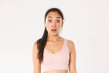 Spor, refah ve aktif yaşam tarzı konsepti. Şaşırmış ve ürkmüş Asyalı fitness kızı, sporcu kadın düşük çeneli, işitme engelli, beyaz arka plan