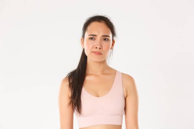 Spor, refah ve aktif yaşam tarzı konsepti. Şüpheci ve hoşnutsuz Asyalı sporcu kadın, kadın atlet sırıtış hayal kırıklığına uğramış ve eğlendirilmemiş, somurtkan yüzlü, beyaz arkaplan