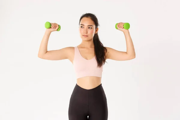 Deporte, bienestar y concepto de estilo de vida activo. Motivado y centrado lindo asiático chica entrenamiento en ropa deportiva, atleta haciendo fitness, levantando pesas y mirar entrenador, ejercicio repetido — Foto de Stock