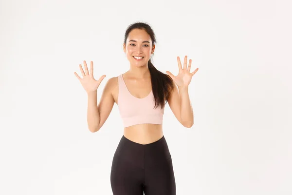 Sport, benessere e stile di vita attivo. Sorridente forte e sottile asiatico femmina istruttore di fitness insegnamento lezione, spiegare dieci passi per il corpo perfetto e allenamento produttivo, sfondo bianco — Foto Stock