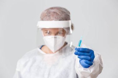 Tıp çalışanları, covid-19 salgını, koronavirüs konsepti. Kişisel koruma ekipmanları içinde ciddi profesyonel kadın doktor, solunum cihazı ve yüz kalkanı takıyor, aşıyla şırınga veriyor.