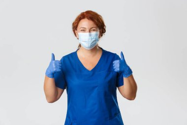 Tıp çalışanları, covid-19 salgını, koronavirüs konsepti. Mutlu gülümseyen hemşire, ameliyat önlüğü giymiş orta yaşlı kadın doktor, tıbbi maske ve eldiven onayı için onay veren eldiven önerin.