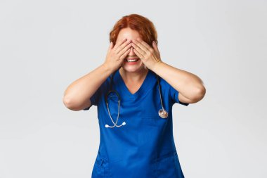 Tıp, sağlık ve koronavirüs konsepti. Neşeli gülümseyen orta yaşlı kızıl saçlı kadın doktor doğum günleriyle, kapalı gözlerle kutlanıyor ve önlük giyip, hediyeler için bekliyor.