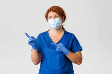 Tıp çalışanları, covid-19 salgını, koronavirüs konsepti. Şüpheci ve eğlendirilmemiş kızıl saçlı kadın doktor, doktor hoşlanmayan, sol üst köşeyi gösteren, etkileyici olmayan bir şey, maske takın.