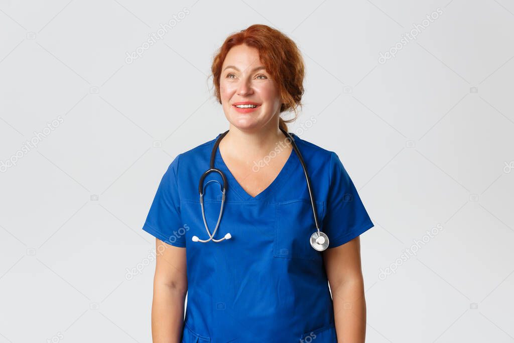 Medicine, healthcare and coronavirus concept. Happy tired medical worker, female nurse in blue scrubs looking upper left corner and smiling dreamy, reading praises for working during pandemic