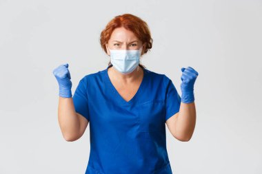 Tıp çalışanları, covid-19 salgını, koronavirüs konsepti. Üzgün ve hayal kırıklığına uğramış kadın doktor gergin görünüyor, baskı altında, bir şeyler bekliyor, kötü haberler alıyor, hoşnutsuzca yumruk sallıyor.